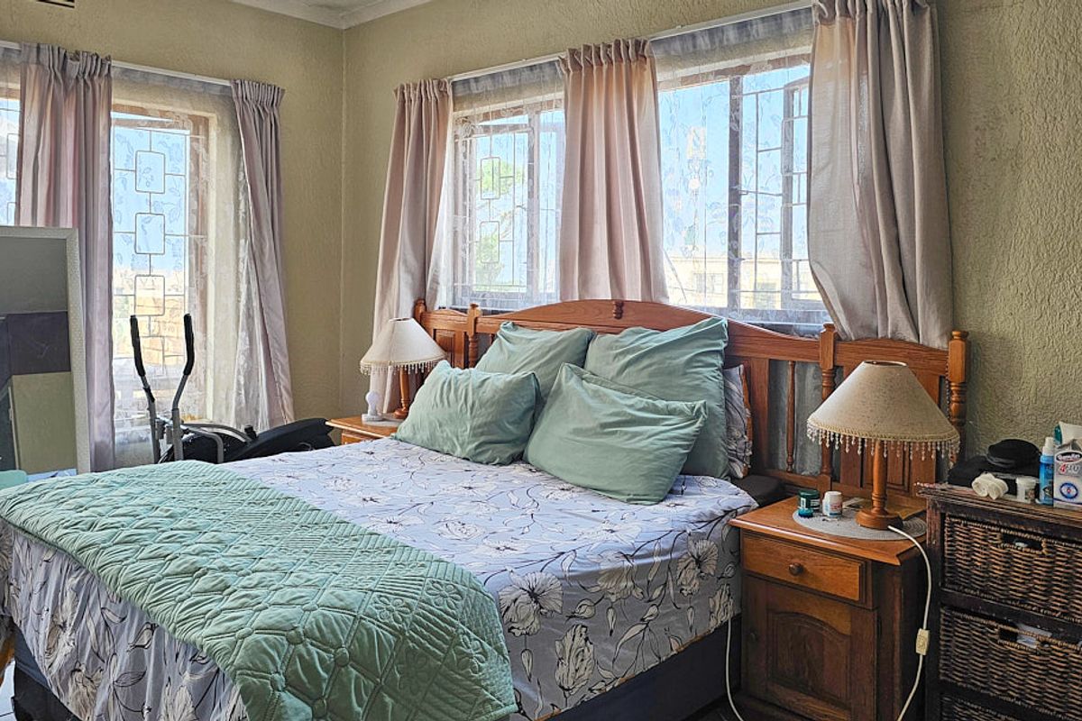 A bedroom featuring tiled flooring, security bars on the windows, and natural light, offering a functional space ready for cosmetic updates.
