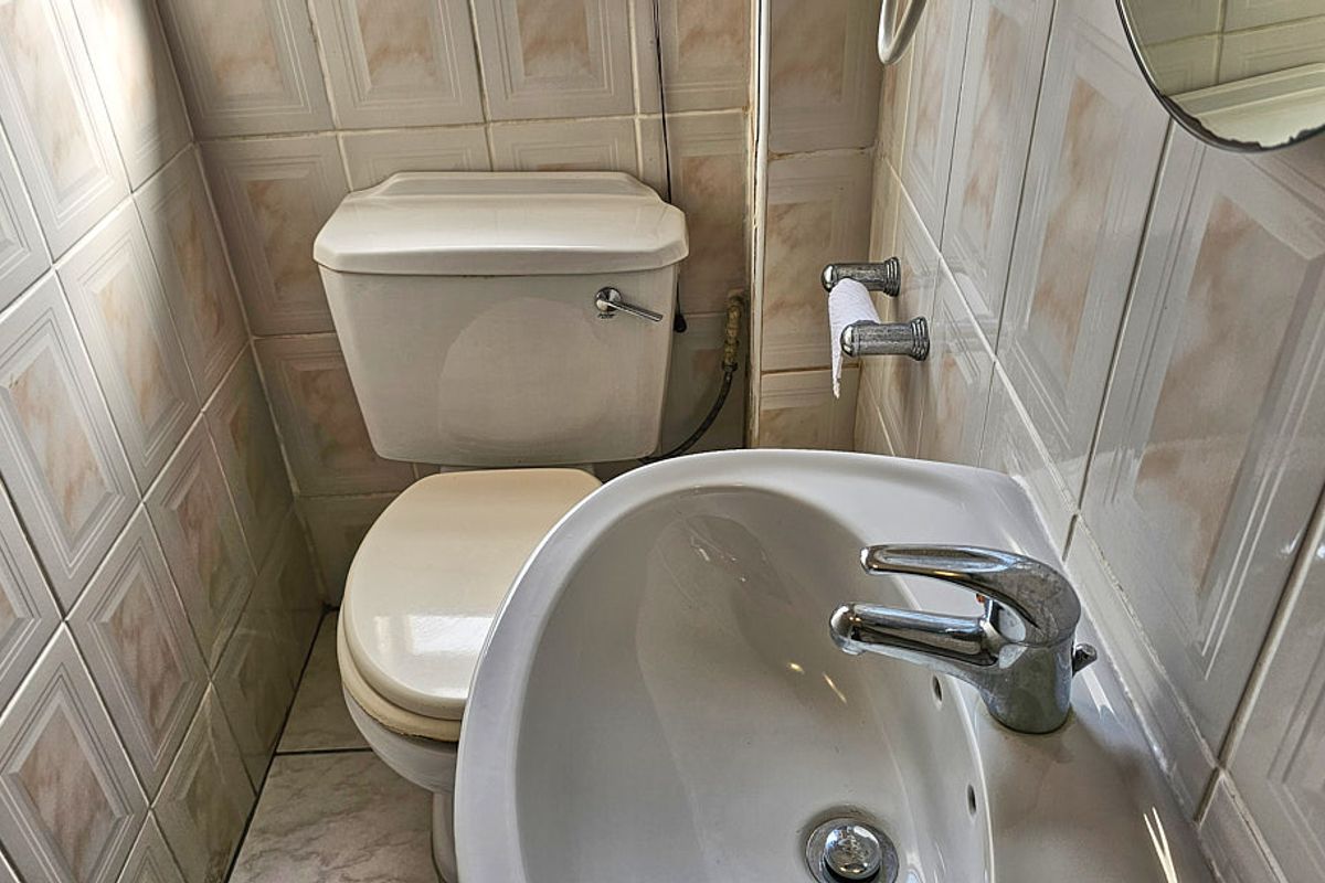A compact bathroom featuring a standard toilet and a wall-mounted washbasin with chrome faucet, finished with dated wall tiling.