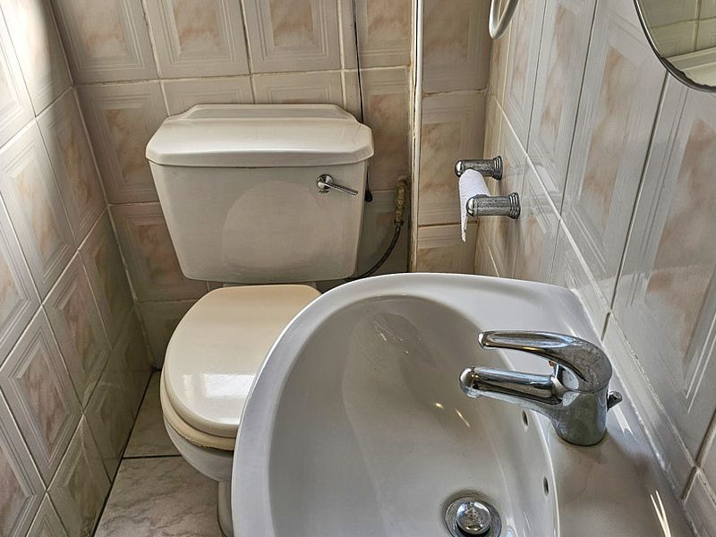 A compact bathroom featuring a standard toilet and a wall-mounted washbasin with chrome faucet, finished with dated wall tiling.