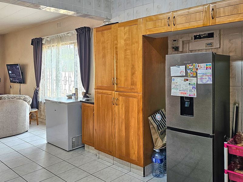 Open-plan living and kitchen area featuring tiled flooring and built-in wooden cabinetry with a tiled splashback.