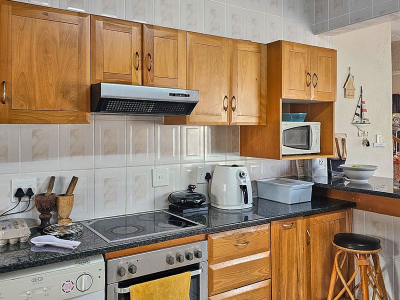 A functional kitchen featuring wooden cabinetry, granite countertops, a built-in oven with an electric hob, and a convenient breakfast bar area.