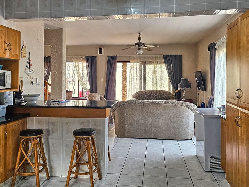 Open-plan living area featuring a kitchen with wooden cabinetry, granite countertops, and a breakfast bar, flowing into a spacious lounge with sliding door access.