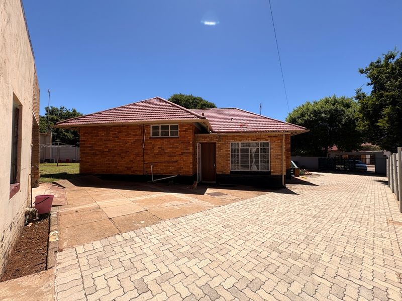 Rear view of a brick house featuring a tiled roof and extensive paved driveway area.