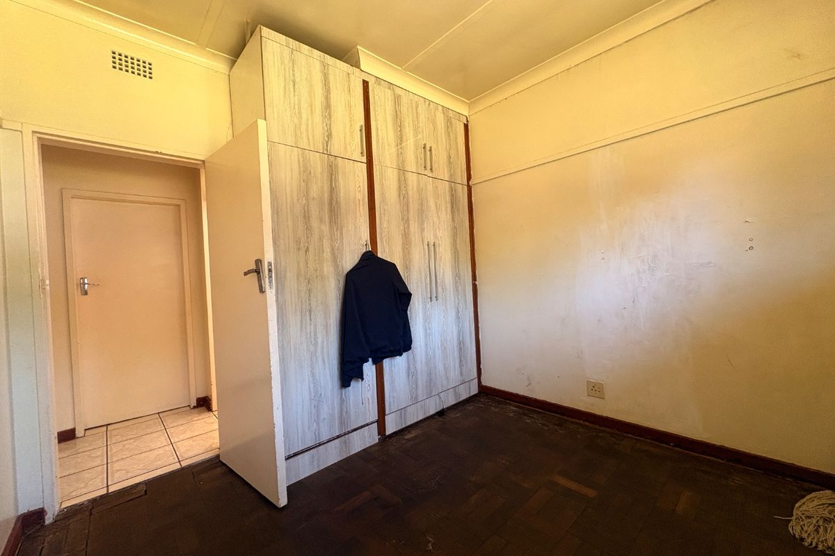 A bedroom featuring built-in cupboards, parquet flooring, and coved ceilings. The room requires cosmetic updates to the walls and flooring.