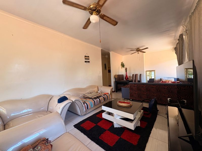 A spacious living room featuring tiled flooring, coved ceilings, and dual ceiling fans, offering a functional layout for comfortable family living.