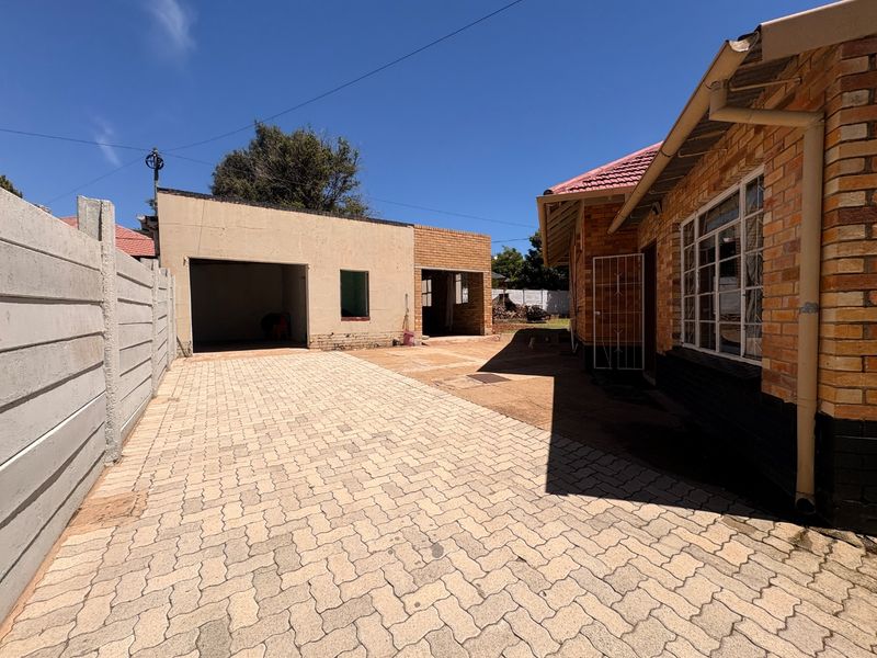 Rear exterior view featuring a paved driveway, detached garage structure, and brick house facade with precast boundary walling.