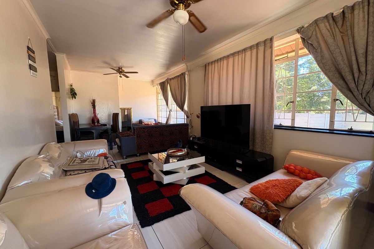 A spacious living room featuring tiled flooring, ceiling fans, and large windows that provide ample natural light, creating a comfortable and functional living space.