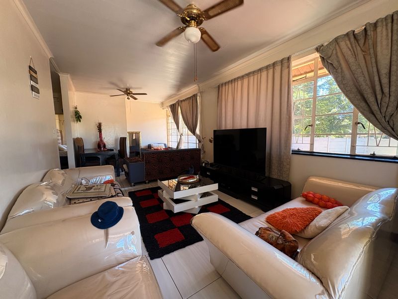 A spacious living room featuring tiled flooring, ceiling fans, and large windows that provide ample natural light, creating a comfortable and functional living space.
