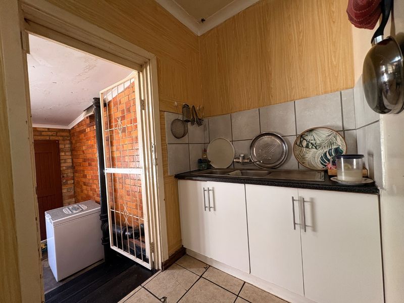 A functional scullery area featuring built-in cabinetry, a stainless steel sink, and tiled splashbacks, providing additional utility space adjacent to the main living area.