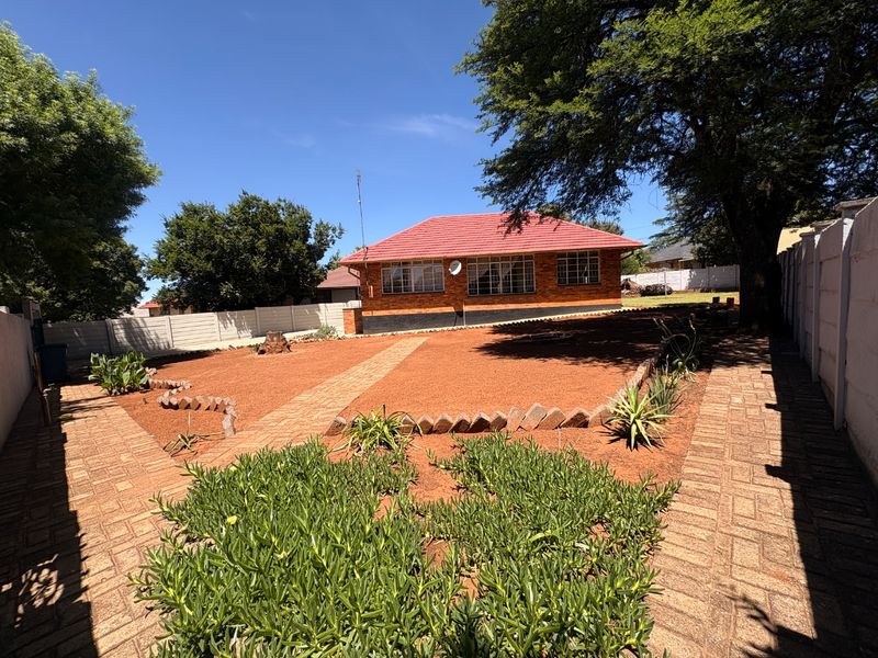 Rear view of a brick house with a tiled roof, featuring a landscaped garden with paved walkways and precast boundary walls.