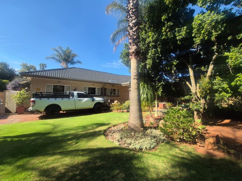 Front elevation of a residential property featuring a tiled roof, brick driveway, and a well-maintained garden with mature trees.