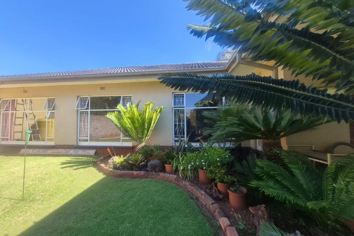 A well-maintained rear exterior view of the house featuring a manicured lawn, landscaped garden beds with brick edging, and large windows.
