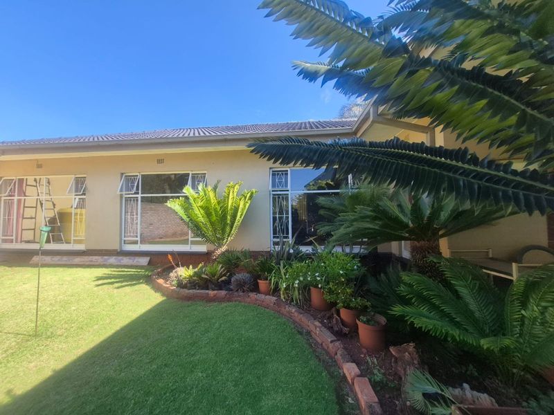 A well-maintained rear exterior view of the house featuring a manicured lawn, landscaped garden beds with brick edging, and large windows.