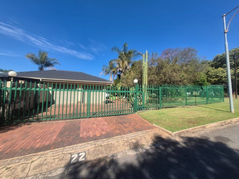 Front view of the property featuring a paved driveway, secure green metal fencing, and a tiled roof facade.
