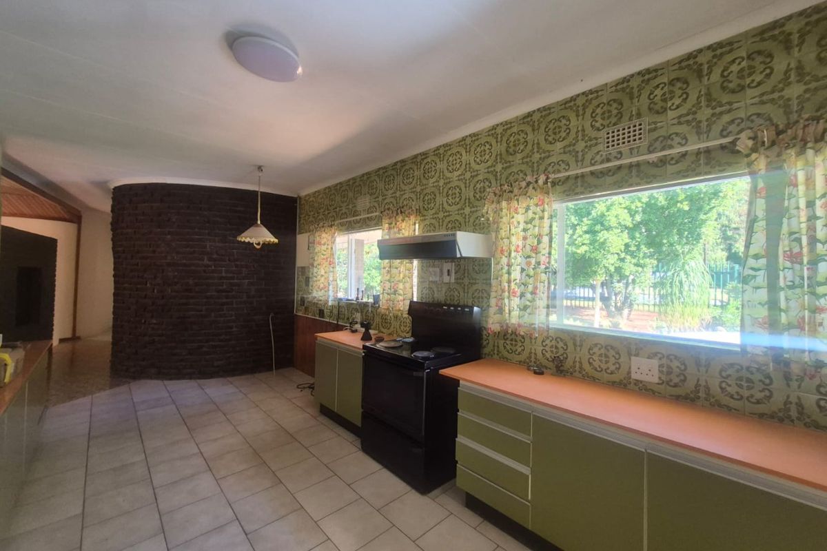 A spacious kitchen featuring dated green cabinetry, patterned wall tiles, an exposed brick feature wall, and tiled flooring with ample natural light.