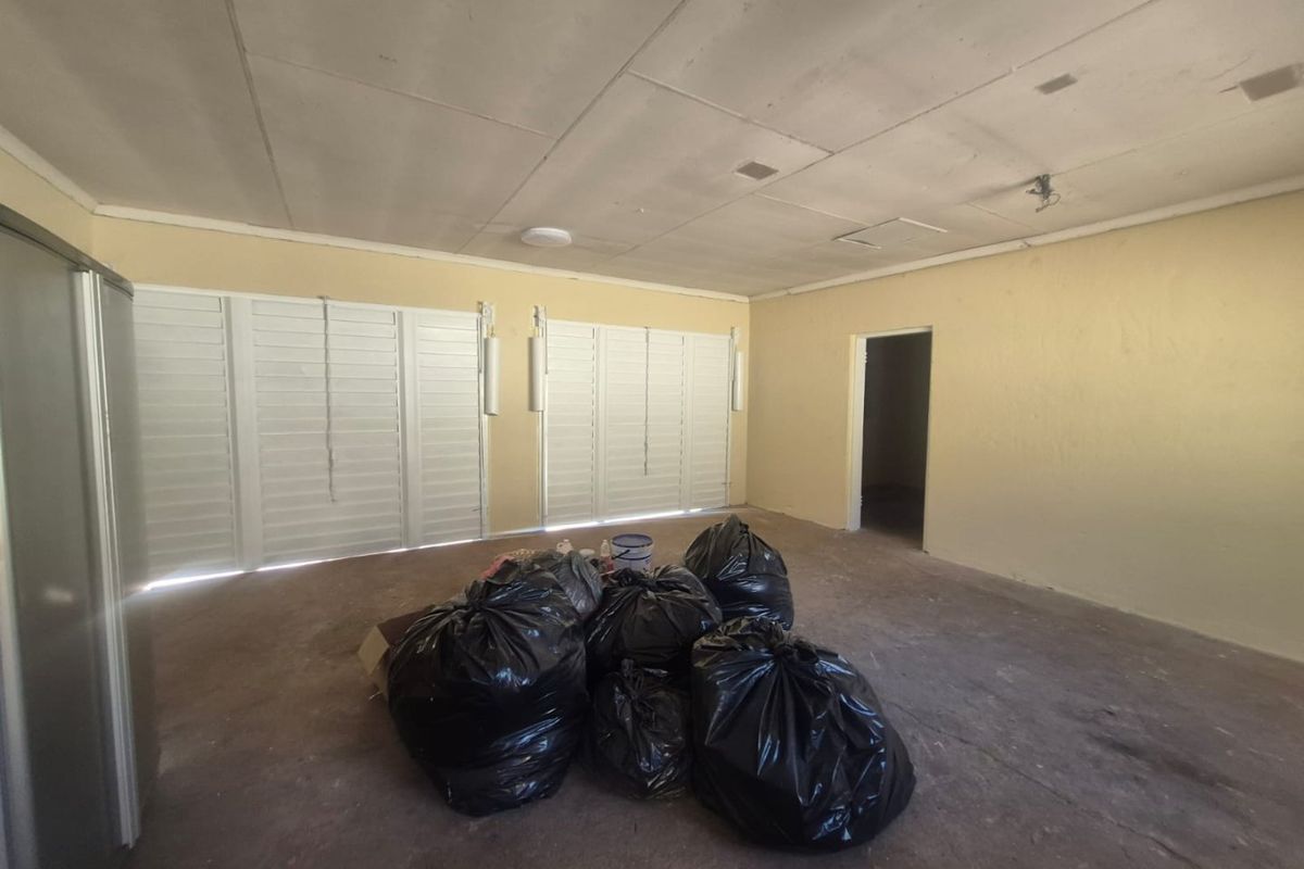 An empty living area featuring white louvre shutters, a tiled ceiling, and neutral wall finishes, offering a blank canvas for renovation.