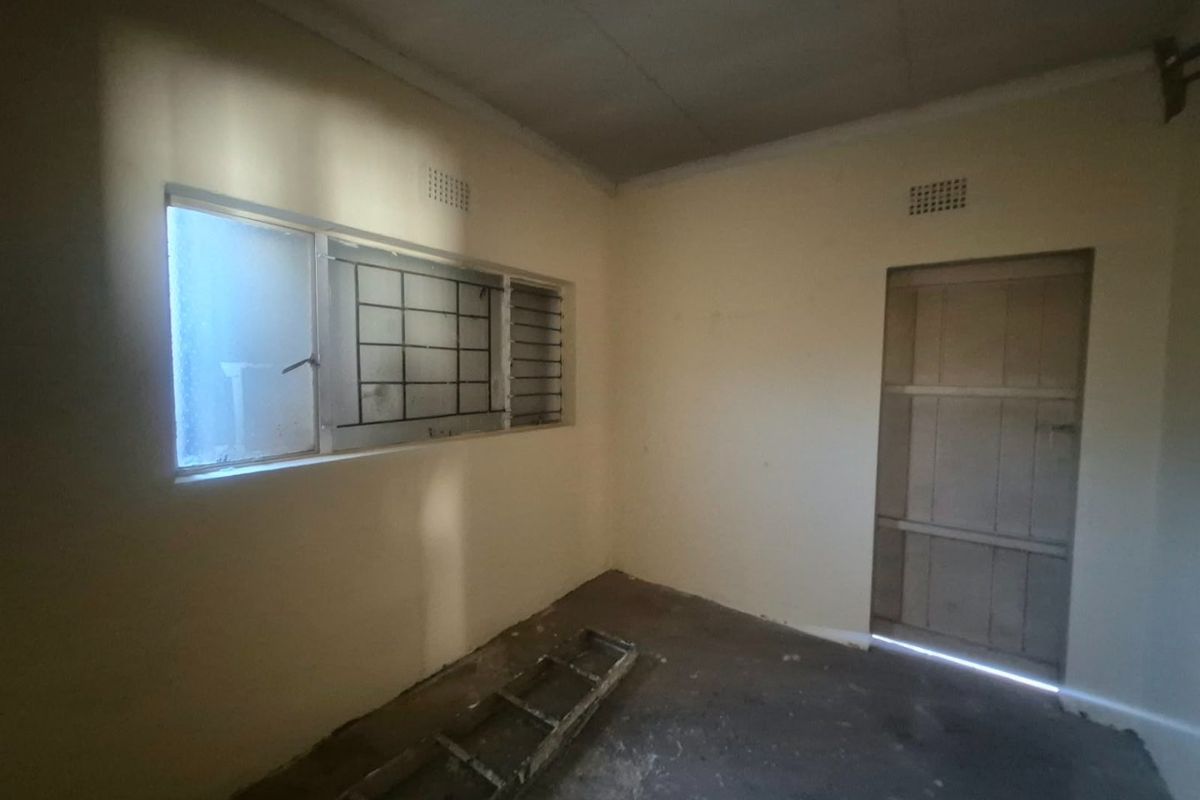 An empty, unfinished bedroom featuring security bars on the window and a timber door, requiring cosmetic updates and flooring installation.