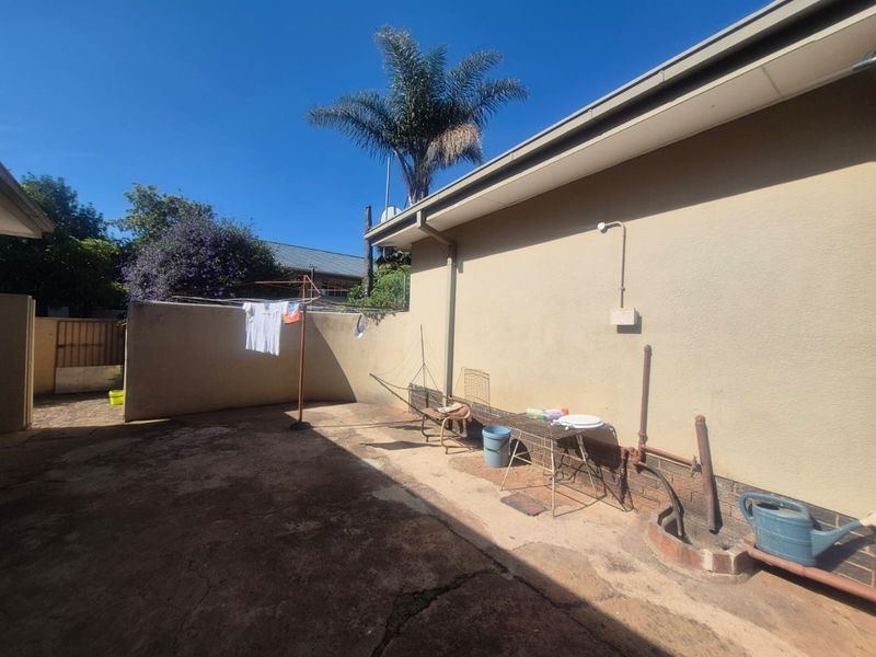 Rear exterior area featuring concrete paving, boundary walls, and external plumbing fixtures, providing a functional utility space.