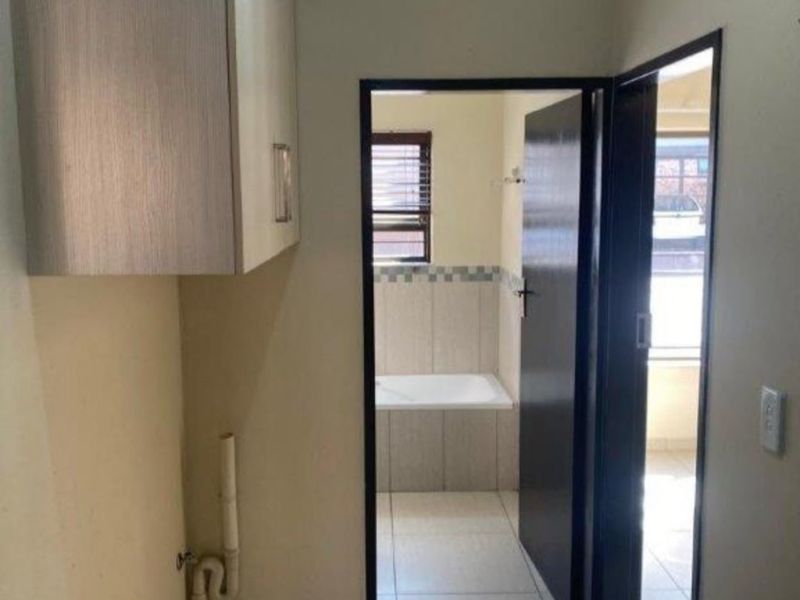 A functional laundry area featuring tiled flooring, wall-mounted cabinetry, and plumbing connections, with a direct view into an adjacent bathroom.