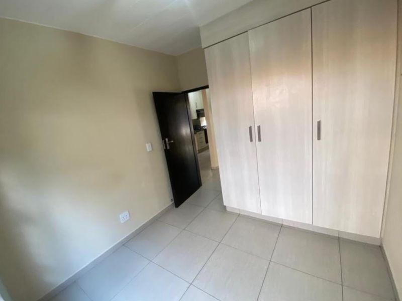 A clean, empty bedroom featuring neutral wall tones, tiled flooring, and built-in storage cupboards.