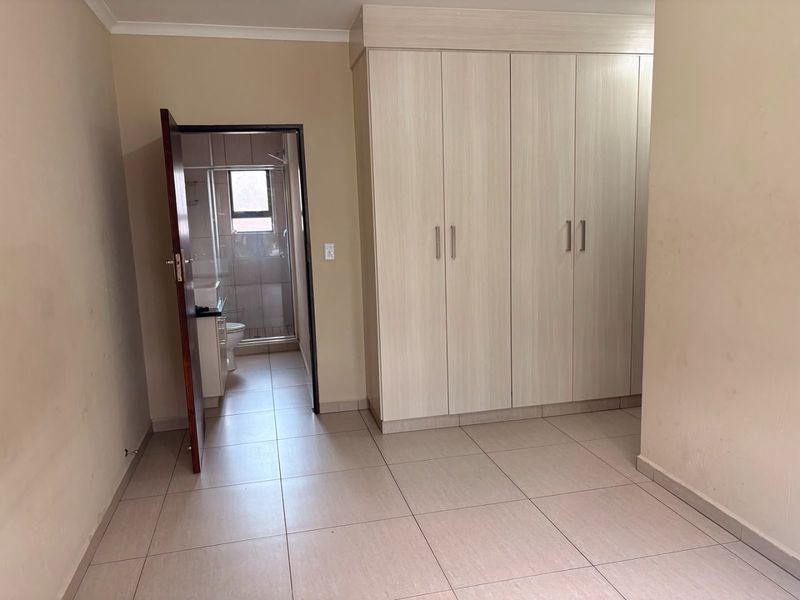 A clean, empty bedroom featuring neutral tiled flooring and modern built-in cupboards, with direct access to an en-suite bathroom.
