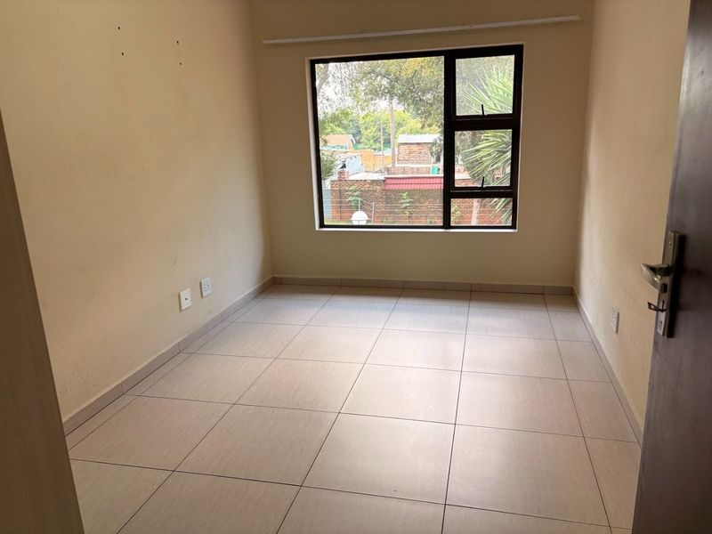 An empty bedroom featuring neutral tiled flooring, clean wall finishes, and a large aluminium-framed window providing natural light.