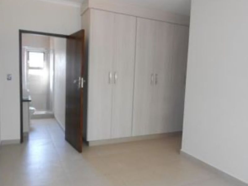 A clean, empty bedroom featuring neutral tiled flooring and ample built-in cupboard storage, with direct access to an adjoining en-suite bathroom.