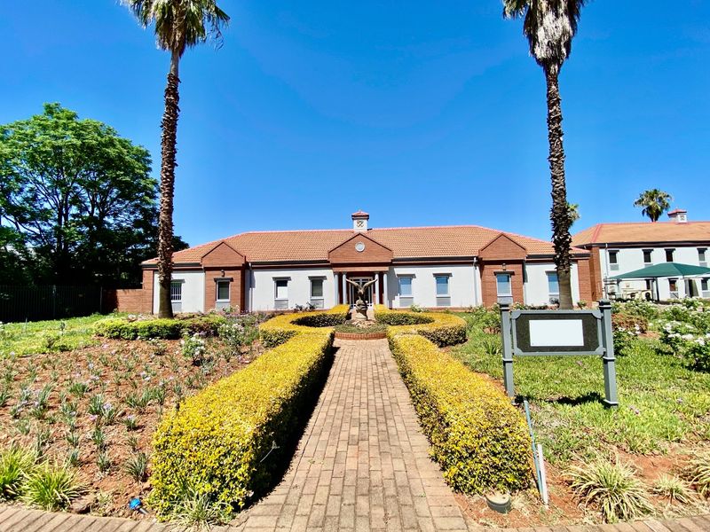 Front view of a commercial property featuring a brick paved walkway leading to the entrance, surrounded by well-maintained landscaped gardens and mature palm trees.