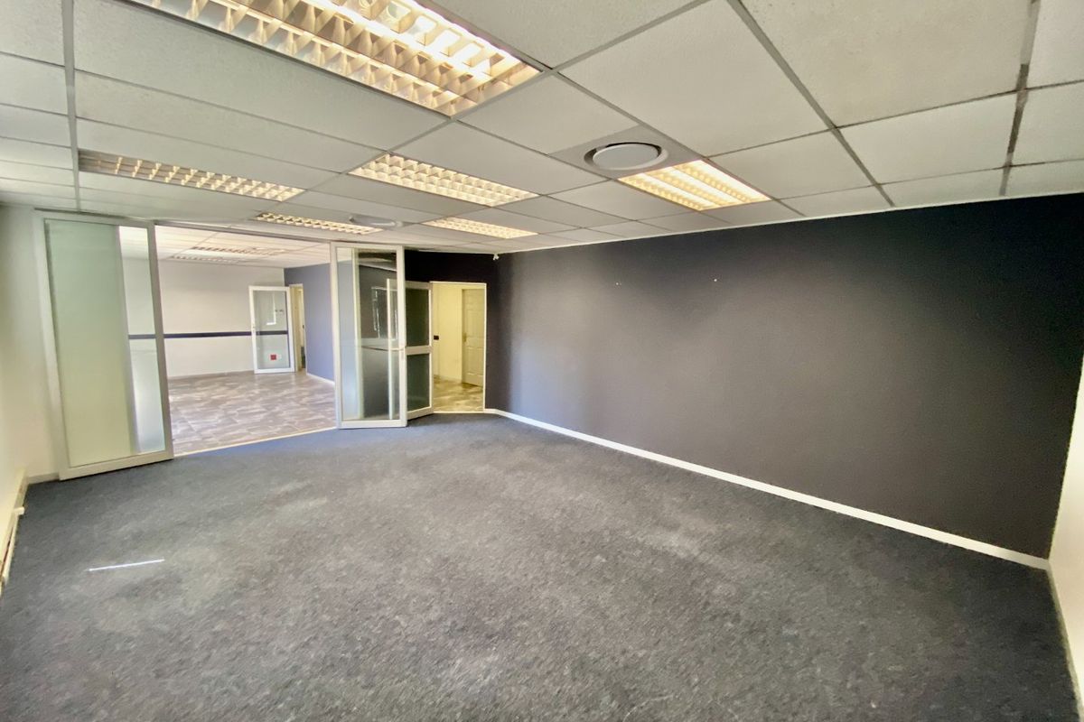 An empty commercial office space featuring a suspended ceiling with recessed lighting, carpeted flooring, and glass partition walls leading to an adjacent room.