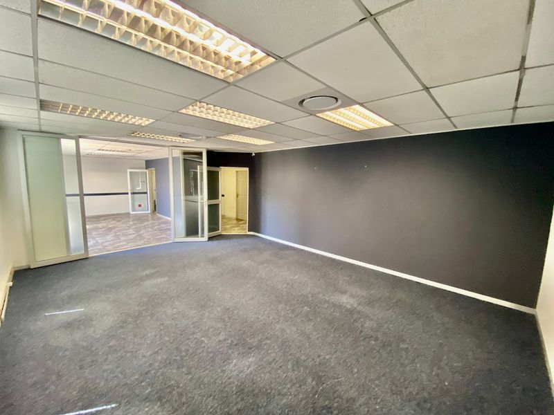 An empty commercial office space featuring a suspended ceiling with recessed lighting, carpeted flooring, and glass partition walls leading to an adjacent room.