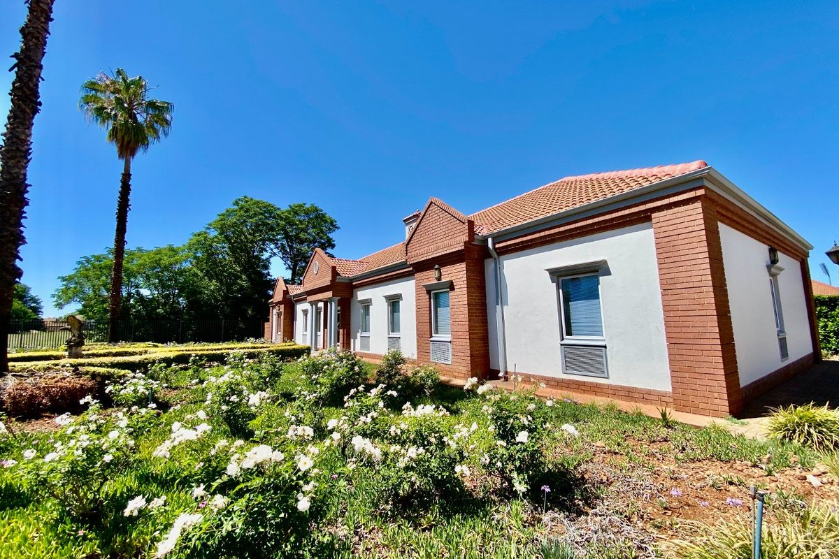 A well-maintained commercial building exterior featuring a classic brick and plaster facade, tiled roof, and established garden surroundings.