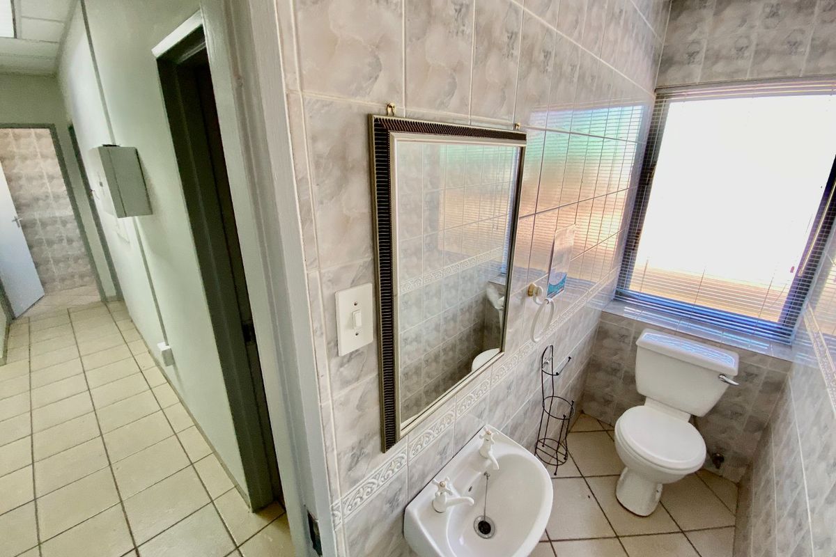 A functional bathroom featuring full-height ceramic wall tiling, a wall-mounted basin, and a standard close-coupled toilet with natural light from a side window.