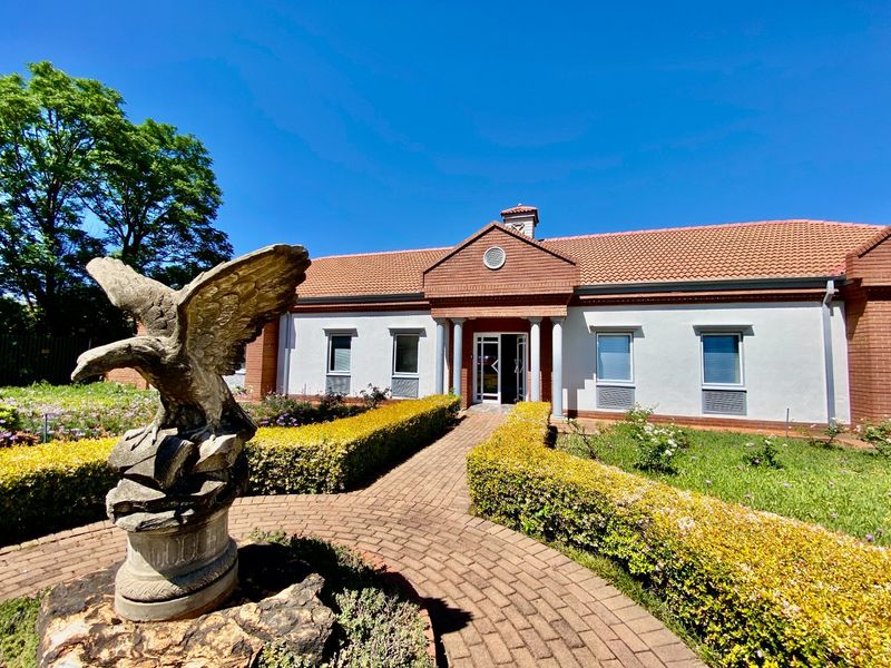 A well-maintained commercial building featuring a brick facade, tiled roof, and a paved walkway leading to a glass entrance, surrounded by landscaped gardens.