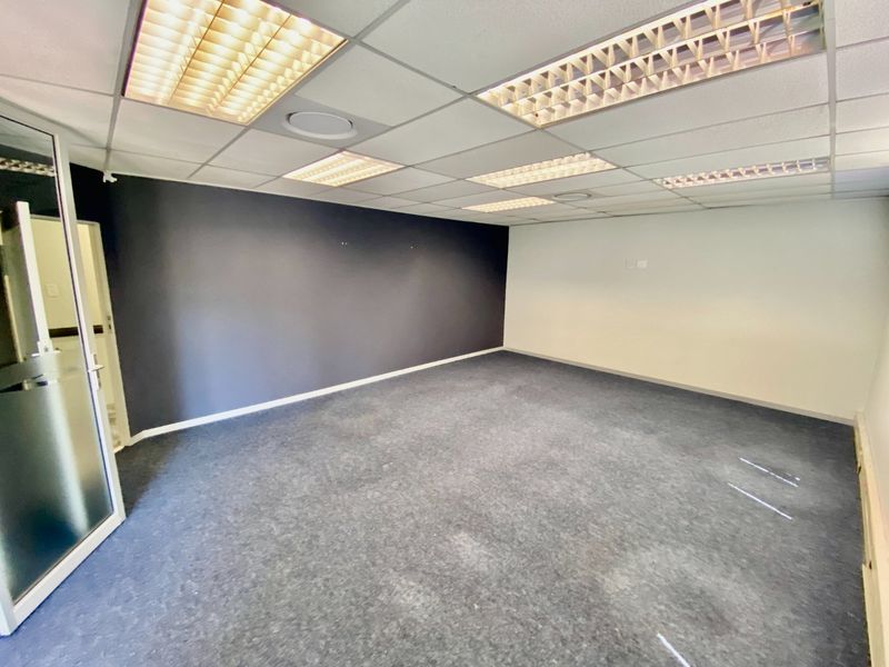 An empty commercial office space featuring a suspended ceiling with recessed lighting, carpeted flooring, and a glass entrance door.