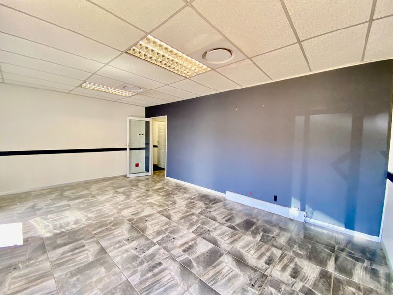 A vacant commercial office space featuring a suspended ceiling with recessed lighting, tiled flooring, and a modern glass-panelled entrance door.