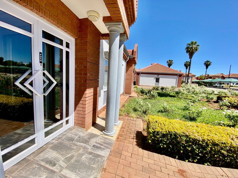 Front entrance of a commercial property featuring a brick facade, decorative columns, stone porch, and a well-maintained landscaped garden area.