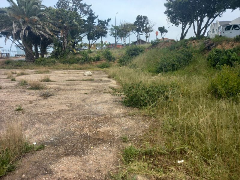 A vacant residential plot featuring a concrete slab foundation and sloped, overgrown terrain in a suburban neighborhood setting.
