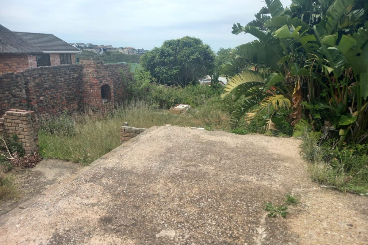 A view of the rear yard featuring a concrete slab, brick boundary wall, and overgrown garden area requiring maintenance.