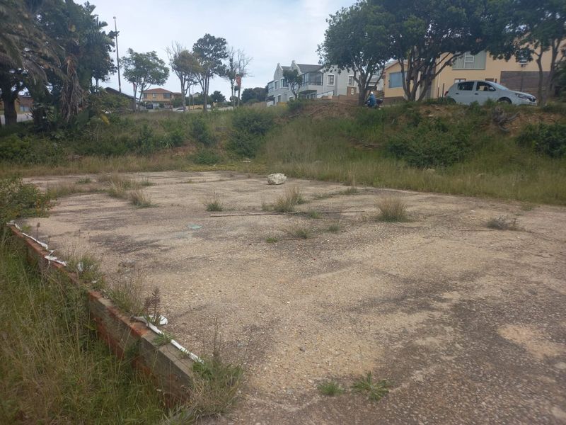 A vacant residential plot featuring an existing concrete slab foundation and a retaining wall, surrounded by established neighborhood vegetation.