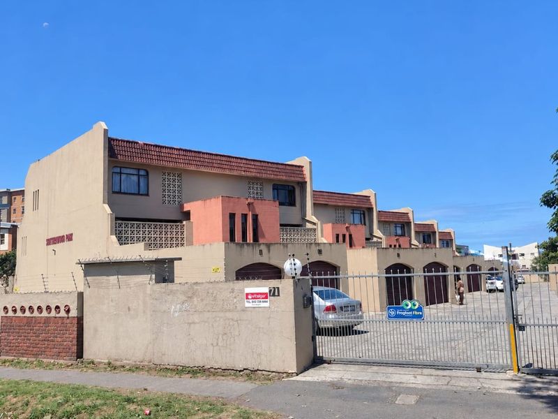 Front elevation of a multi-unit residential complex featuring a secure gated entrance, perimeter wall with electric fencing, and multiple garage access points.