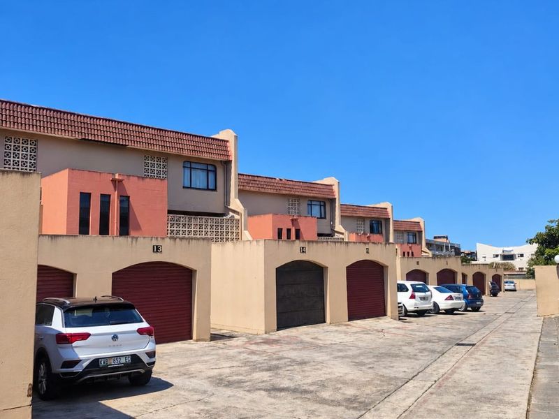 A row of residential townhouses featuring individual garage access, tiled roofing, and a shared concrete driveway in a suburban complex setting.