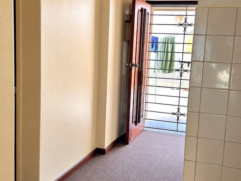 A functional hallway space featuring a security gate, tiled wall accents, and neutral wall finishes, providing access to the exterior.