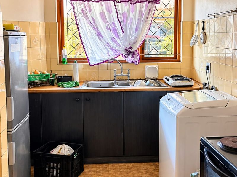 A functional kitchen featuring dark cabinetry, a double sink with chrome tap, tiled splashbacks, and a window with security bars.