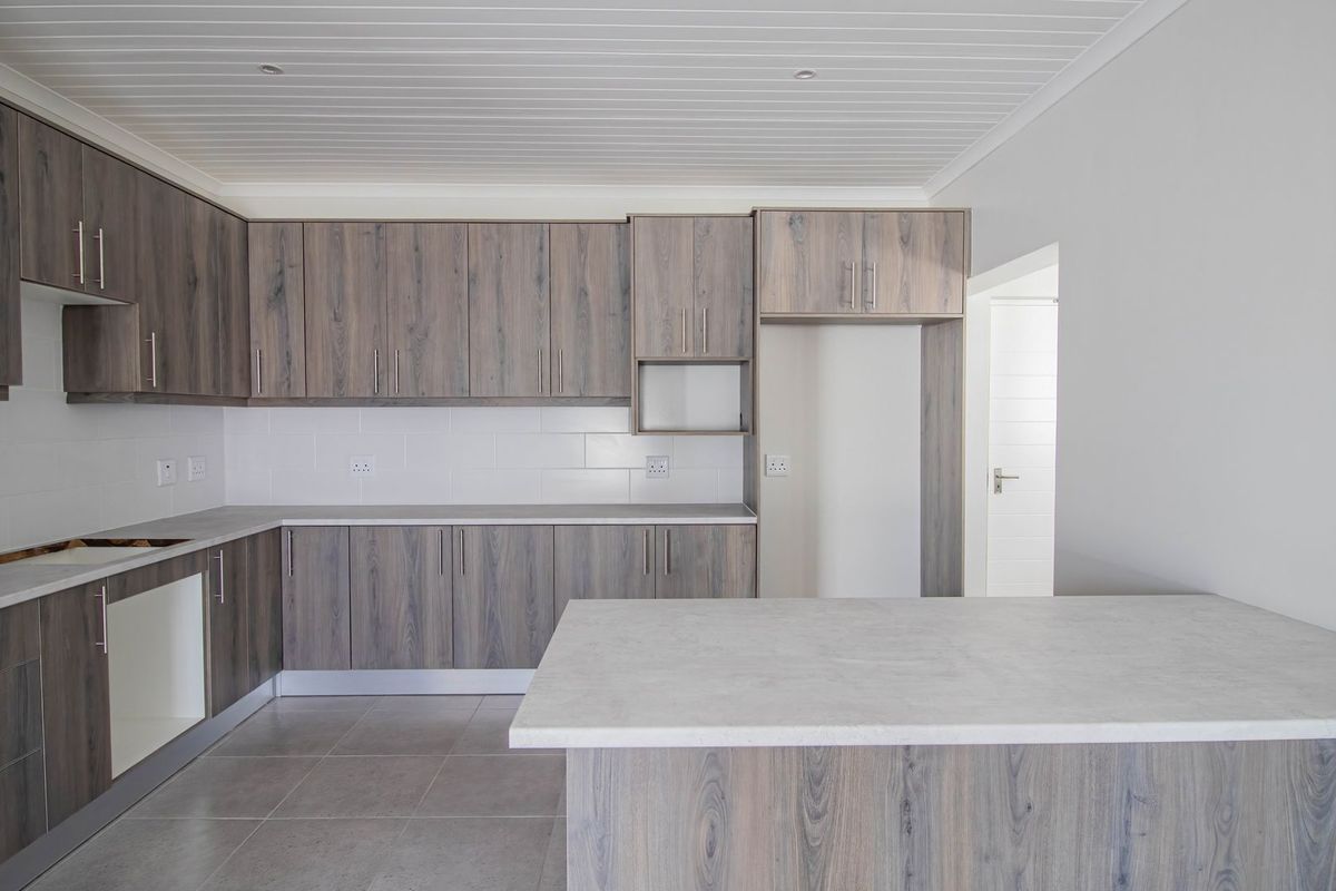 A modern, empty kitchen featuring wood-grain laminate cabinetry, stone-look countertops, subway tile backsplash, and neutral ceramic floor tiles.