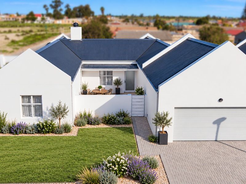 Aerial view of a modern house featuring a corrugated metal roof, paved driveway, integrated garage, and a well-maintained landscaped garden with a covered patio.