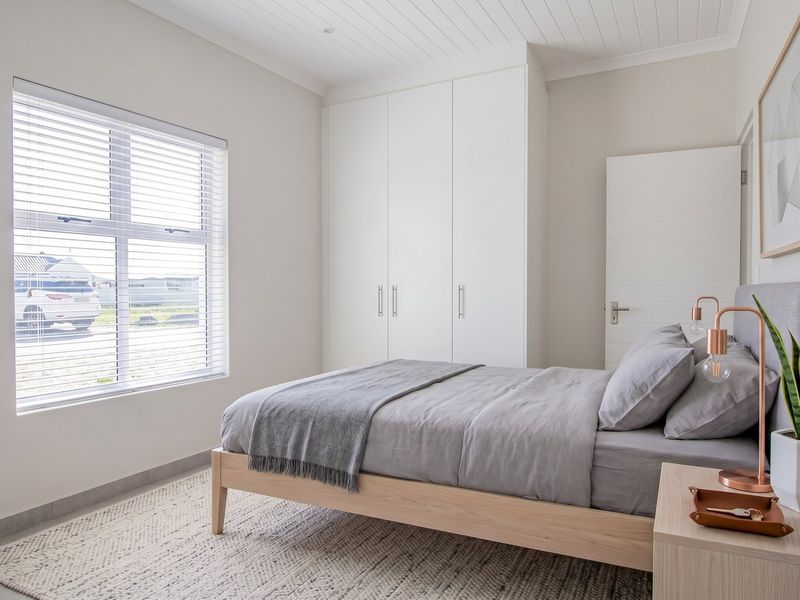A bright and modern bedroom featuring built-in cupboards, tongue and groove ceiling detail, and large windows with venetian blinds.