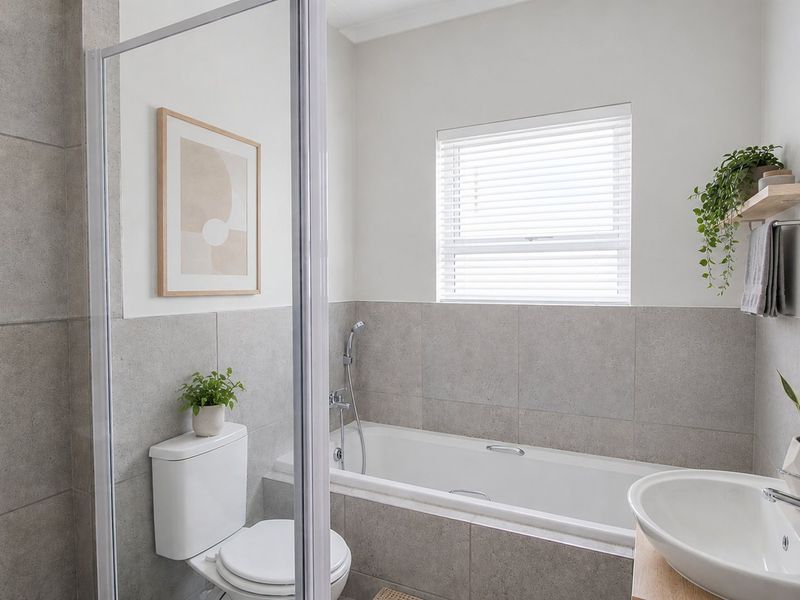 A modern, well-maintained bathroom featuring a built-in bathtub, a separate shower enclosure, a vessel sink, and neutral grey wall tiling.