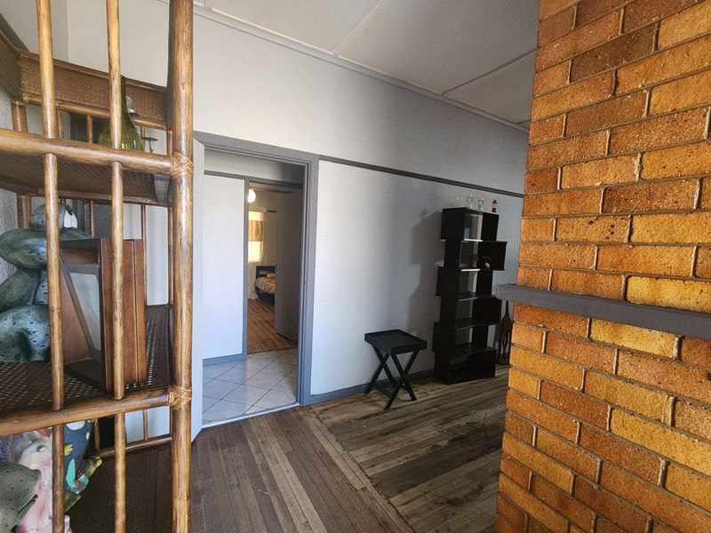 A hallway featuring exposed brickwork and a transition between timber and tiled flooring, leading into an adjacent bedroom.