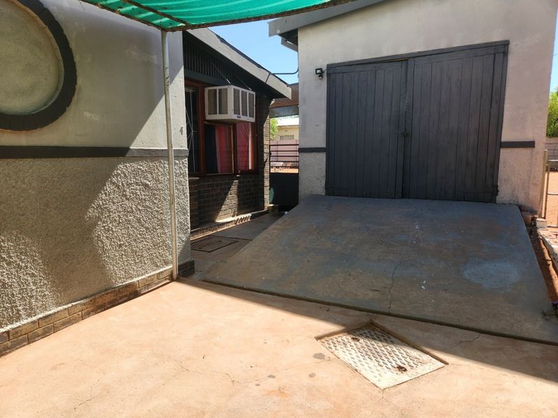Rear exterior area featuring a concrete driveway, garage access, and a shaded patio space with visible wear on finishes.