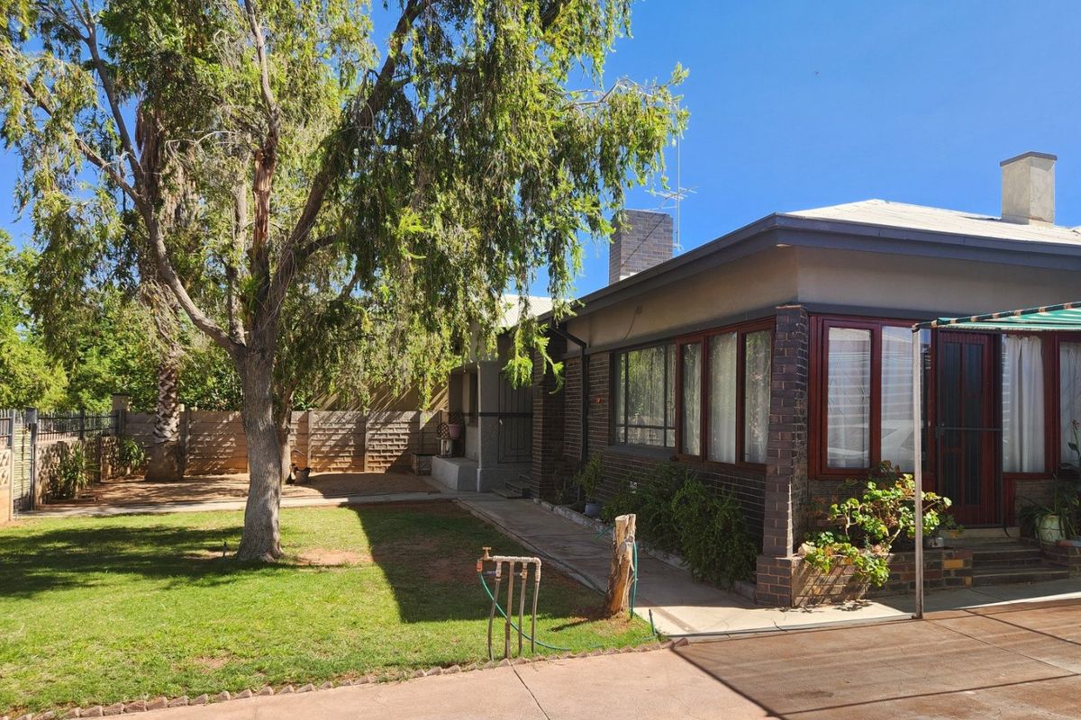 Rear view of the property featuring a brick facade, established lawn, concrete driveway, and chimney, showcasing the outdoor space and building exterior.